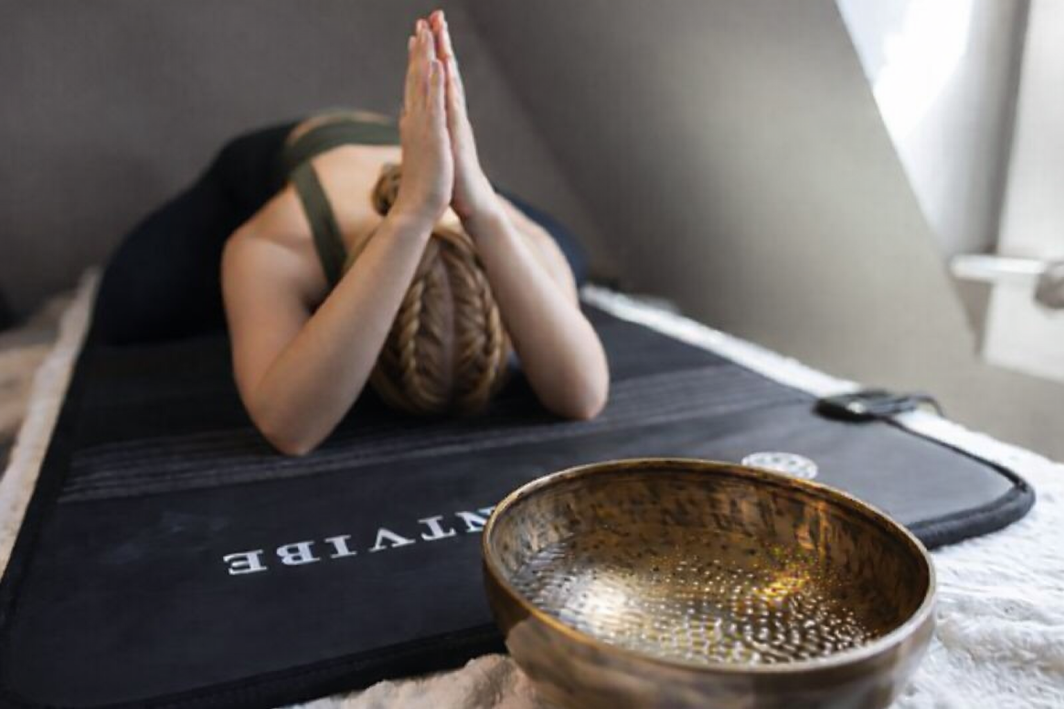 Woman practicing yoga on a VAVE bed during an ActiVAVE session, with cymatic water patterns forming in a bowl from the vibrations of the VAVE bed.